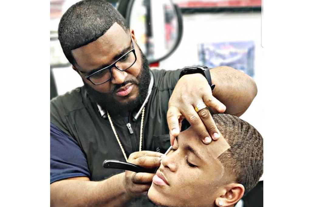 Barber using a straight razor to line up a customer's hairline at Trendsetters Barber Shop